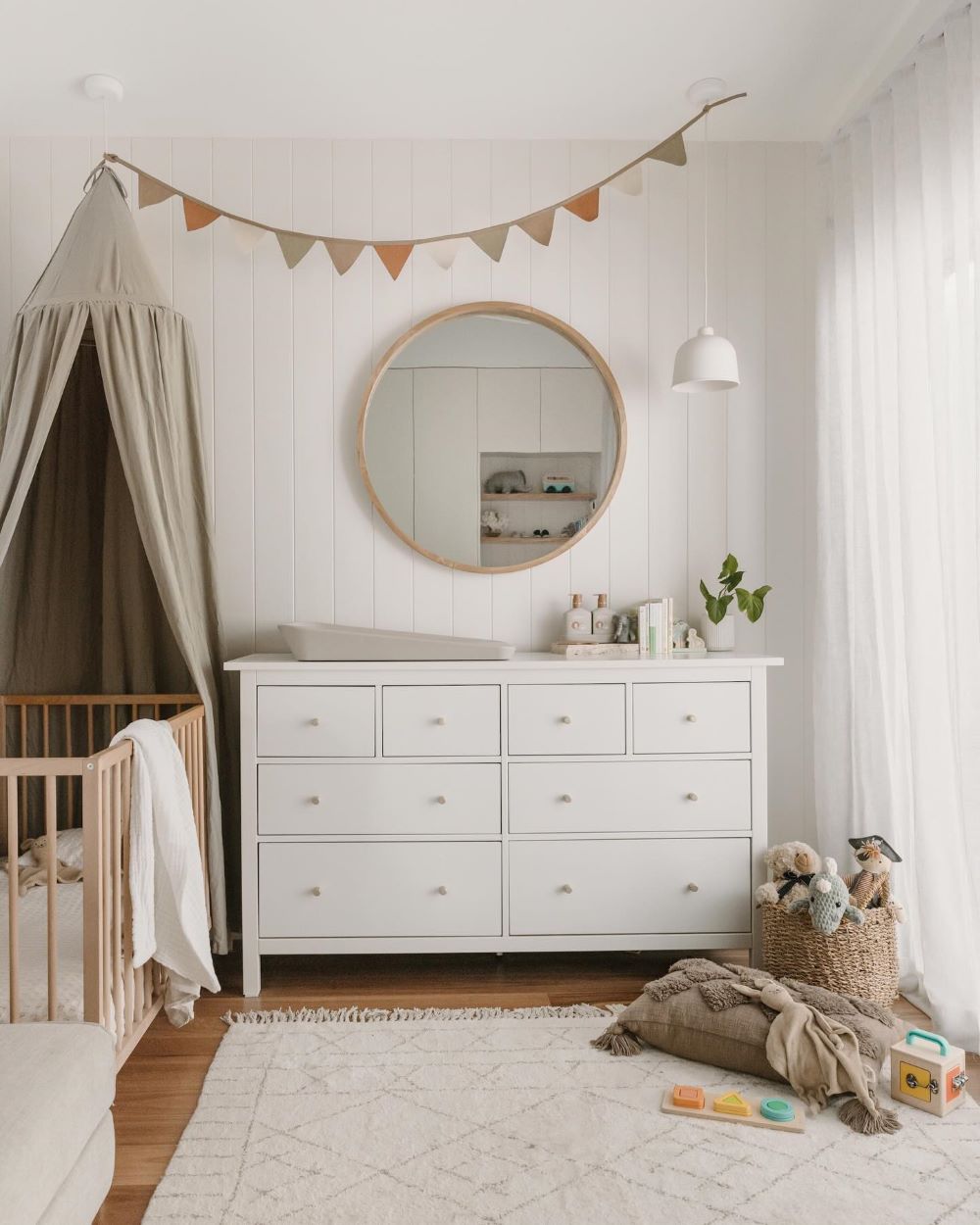 A nursery with white walls and wooden floors featuring white decor, cozy details, and a crib canopy