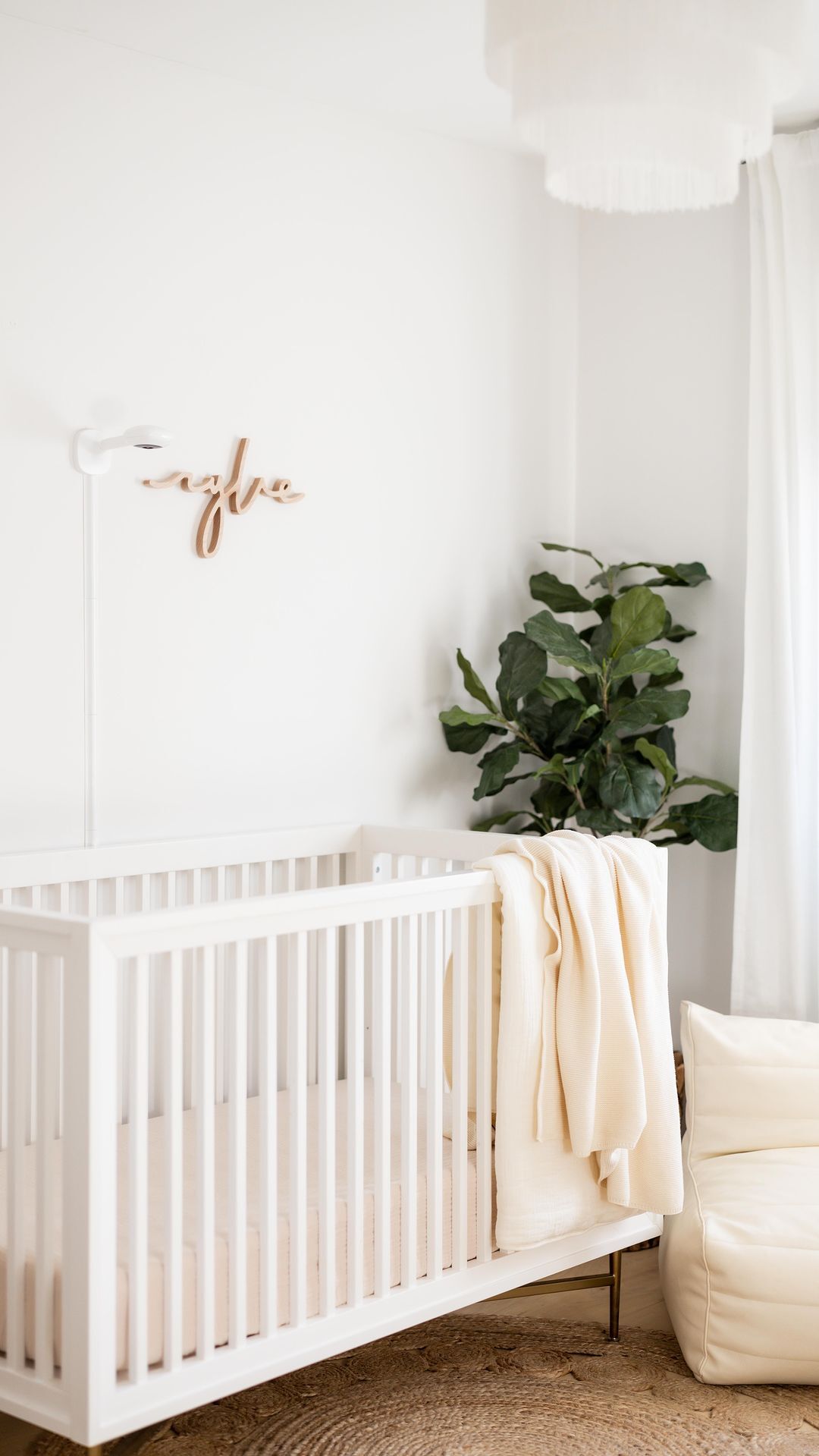 A baby boy nursery with a white crib, a wooden name sign, a white throw blanket, and a dark green plant