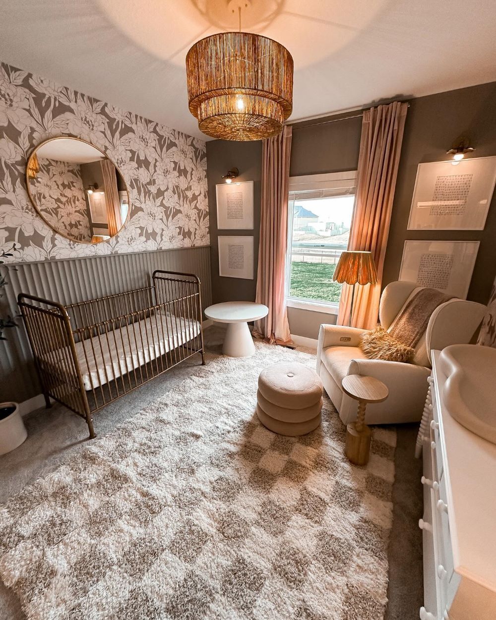 A baby girls white, grey, and beige nursery room with floral wallpaper, a checkerboard rug, a vintage brass crib, and boho decor