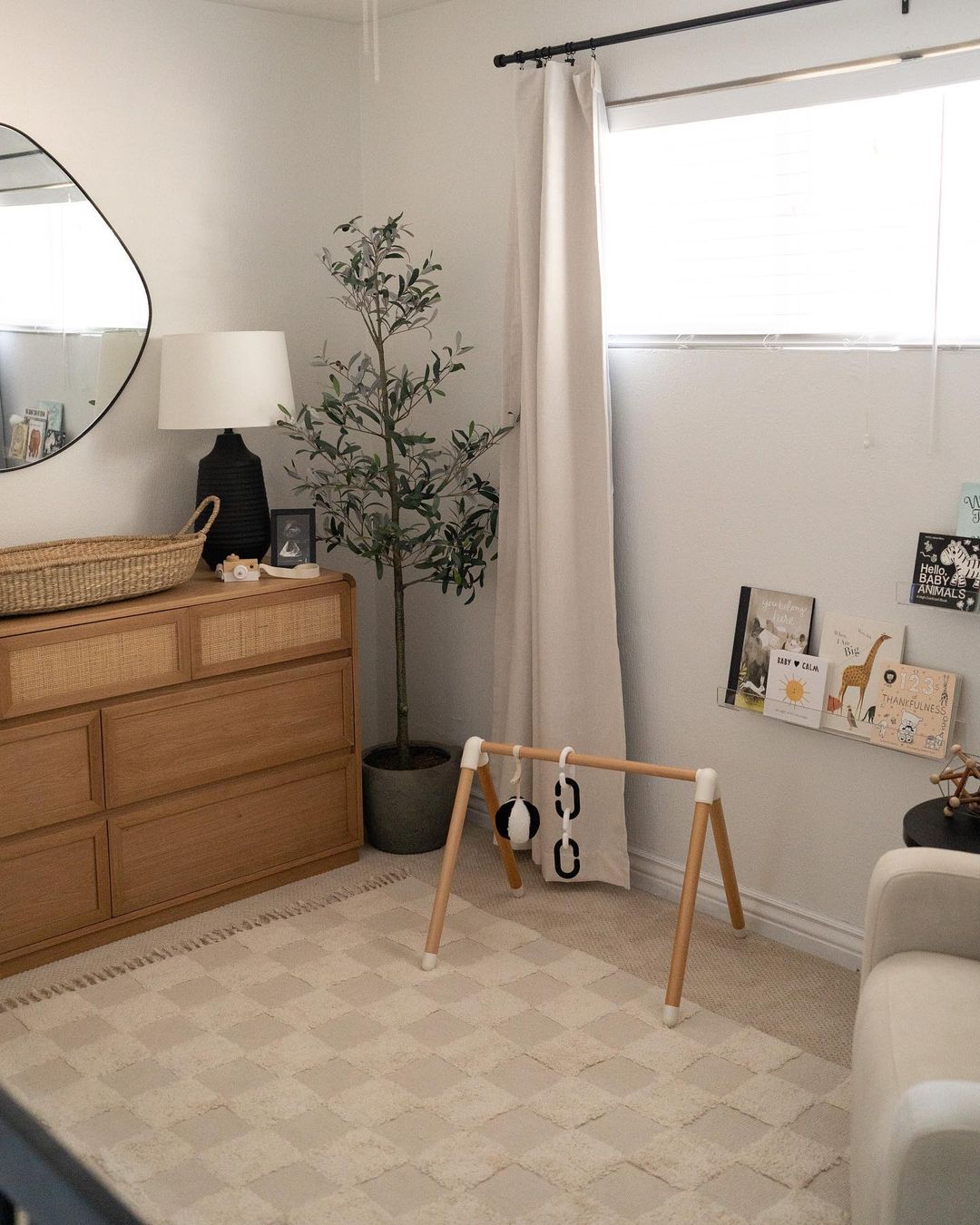 A baby boy nursery room with a checkerboard rug, a faux plant, and white and wood furniture