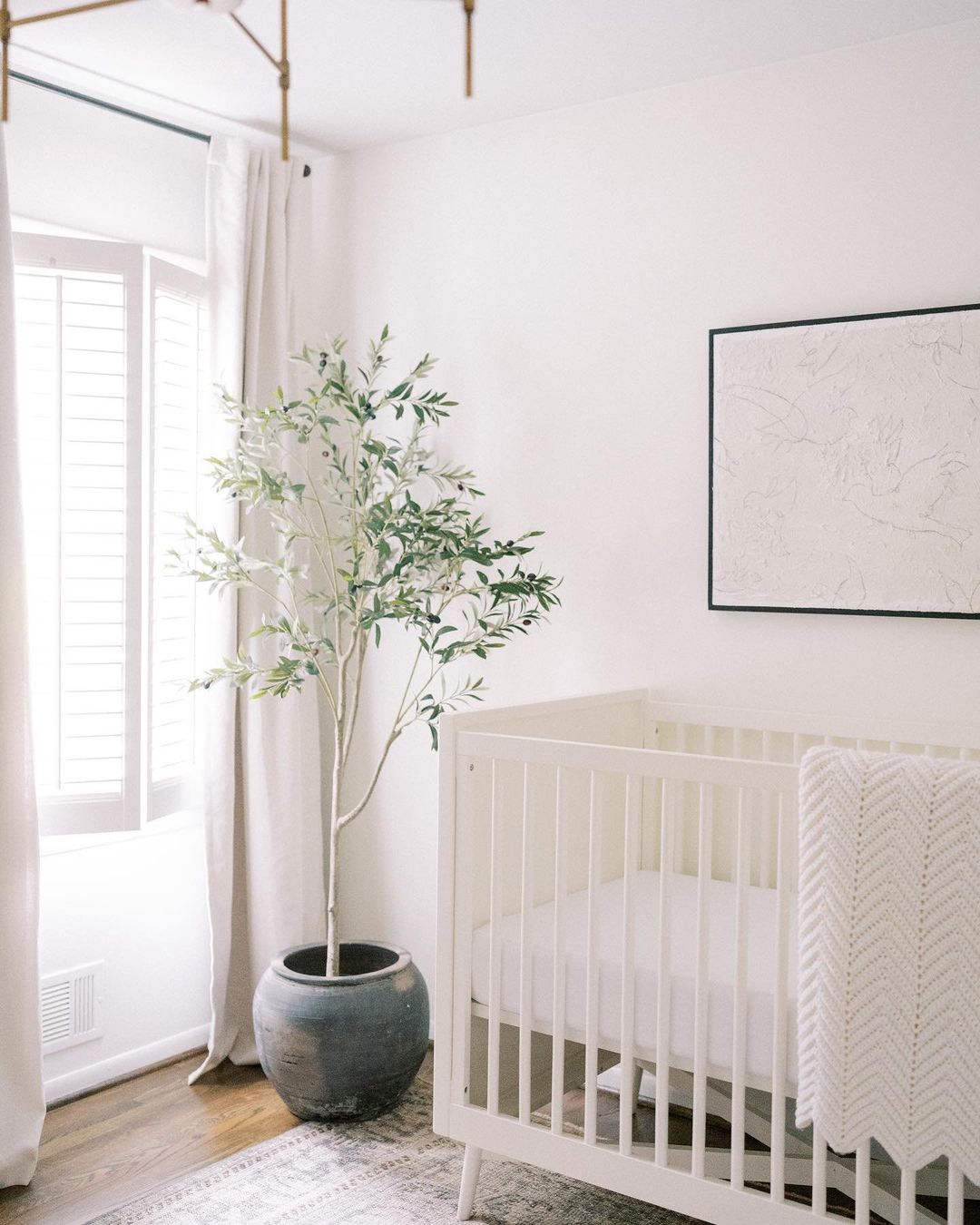A baby boy nursery room with white walls, curtains, and furniture with a faux plant