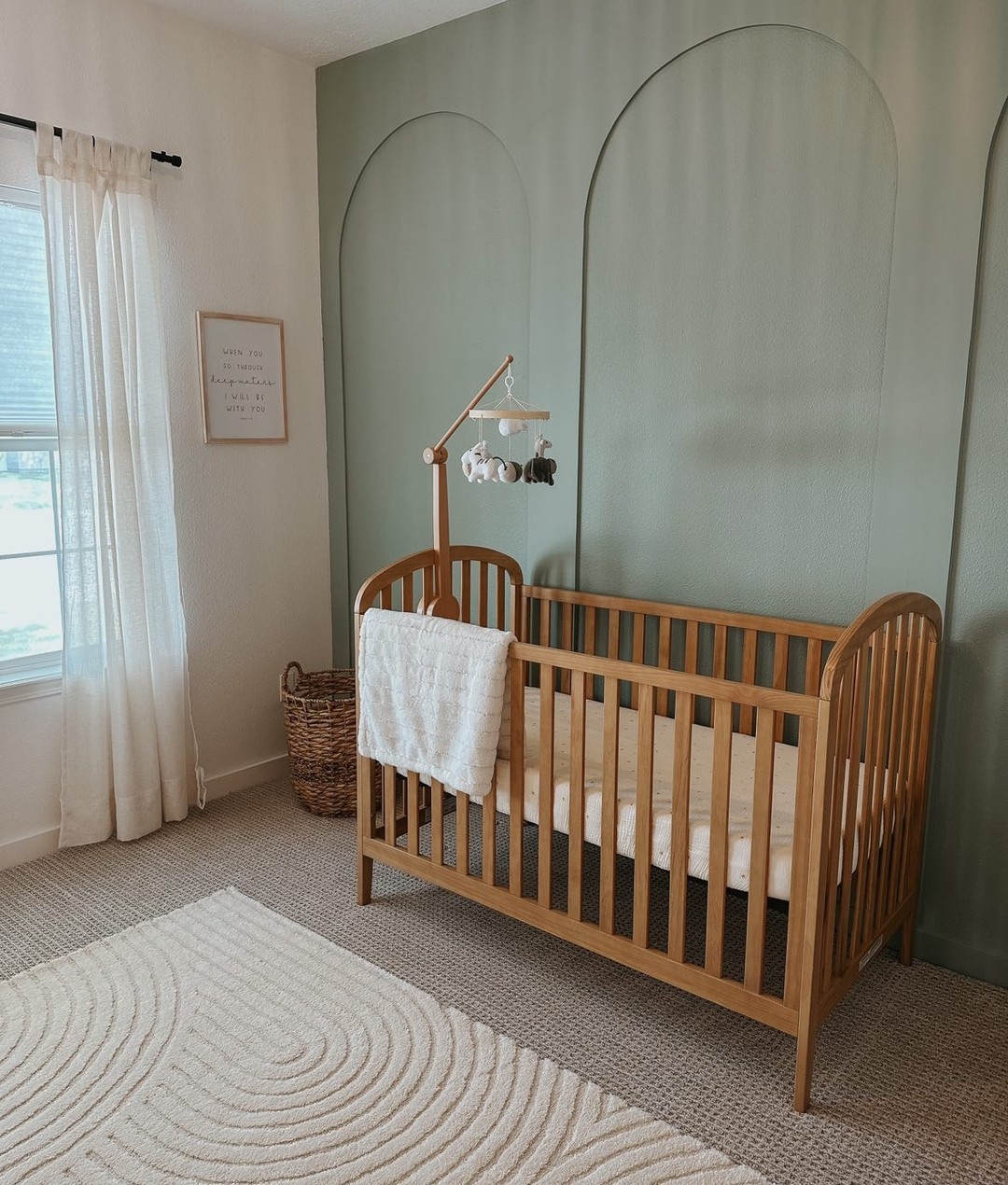 A baby boy nursery room with a green accent wall and subtle boho decor