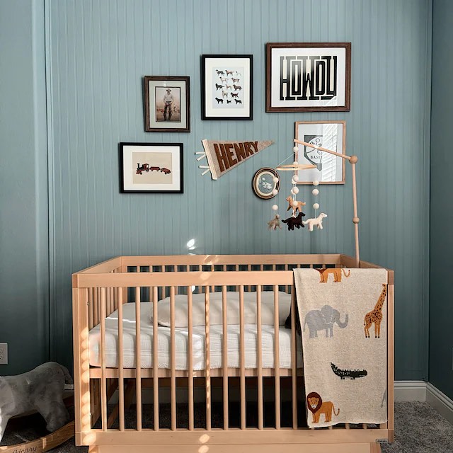 A baby boy nursery room with dusty teal walls, light-toned furniture and a gallery wall