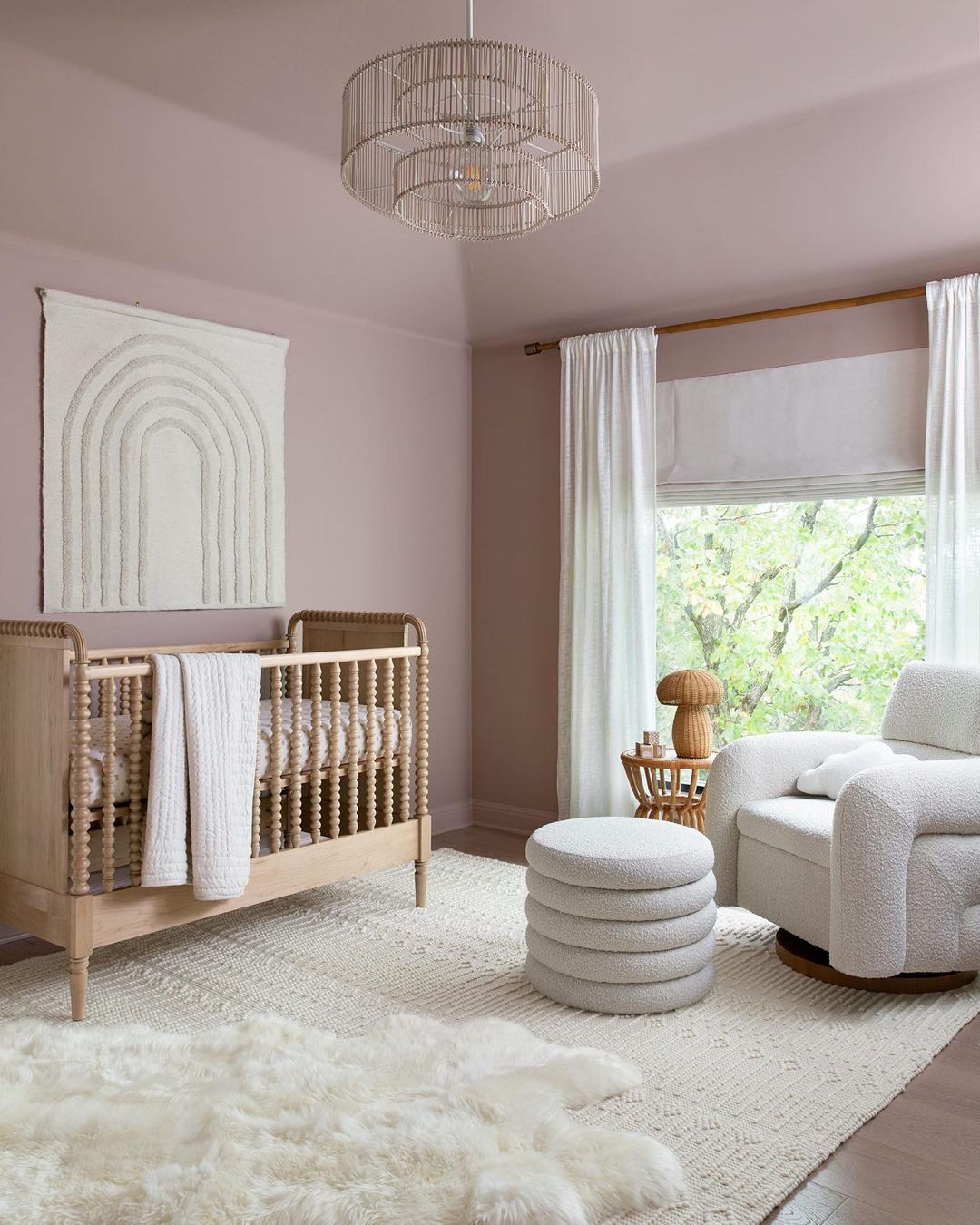 A girl's nursey with light mauve walls, white boucle, and natural wood elements, and boho decor