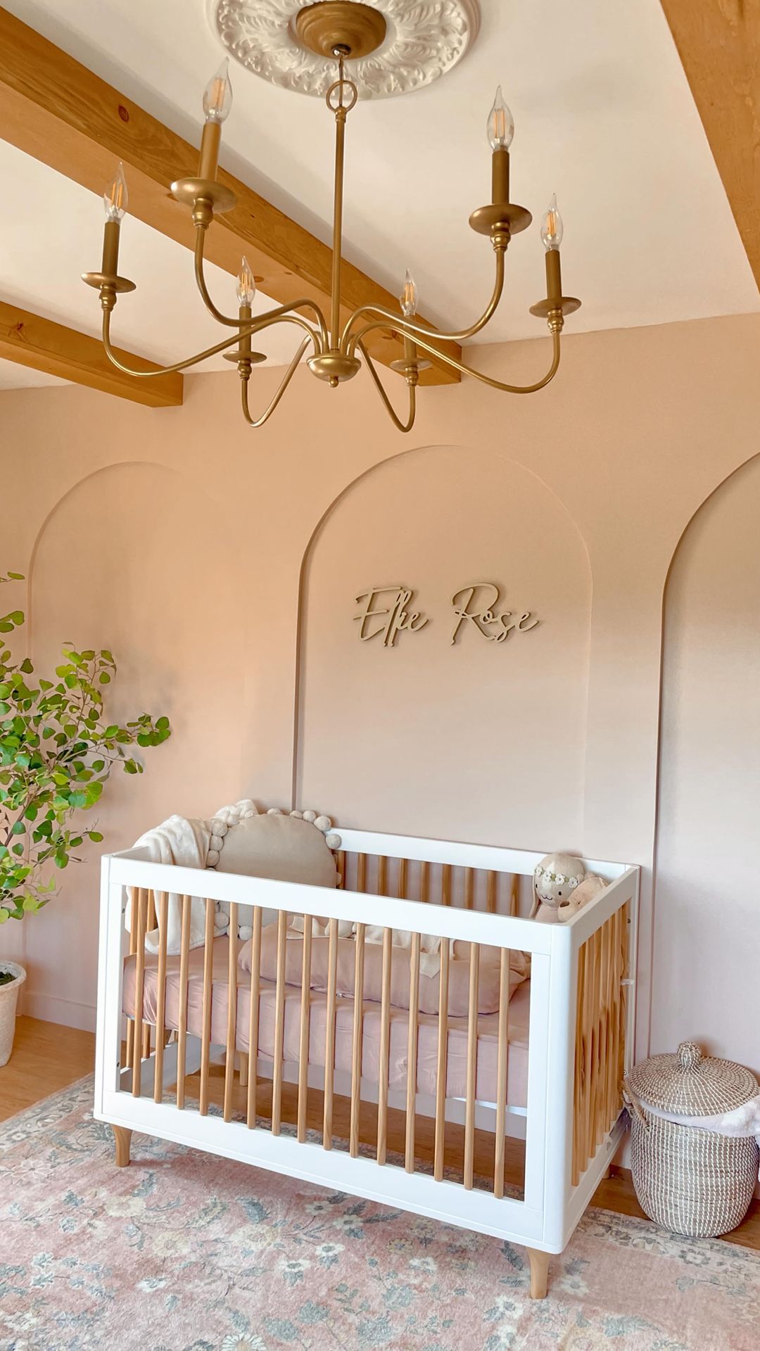 A girls nursery with dusty pink walls and decor pieces, a name sign, and feminine decor