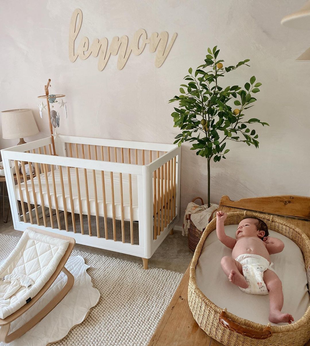 A girls nursery with a wooden name signs, a white crib, soft white and cream tones, and a faux lemon tree