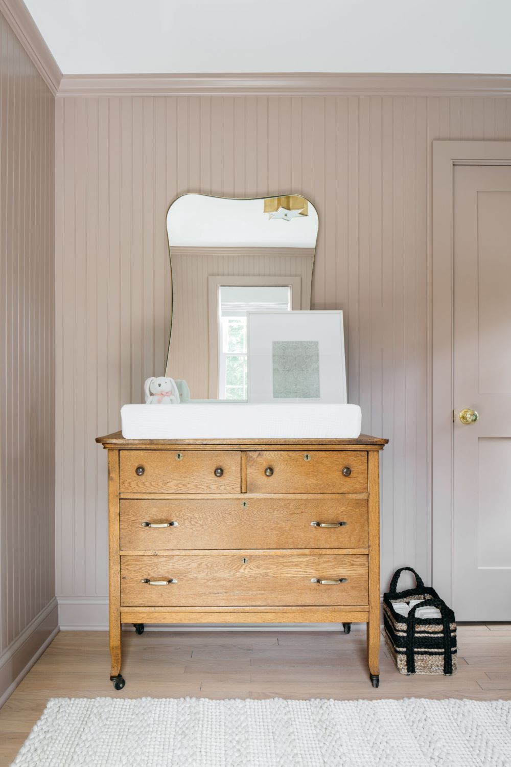 A nursery with soft pink walls, a light wood dresser, and classic decor pieces