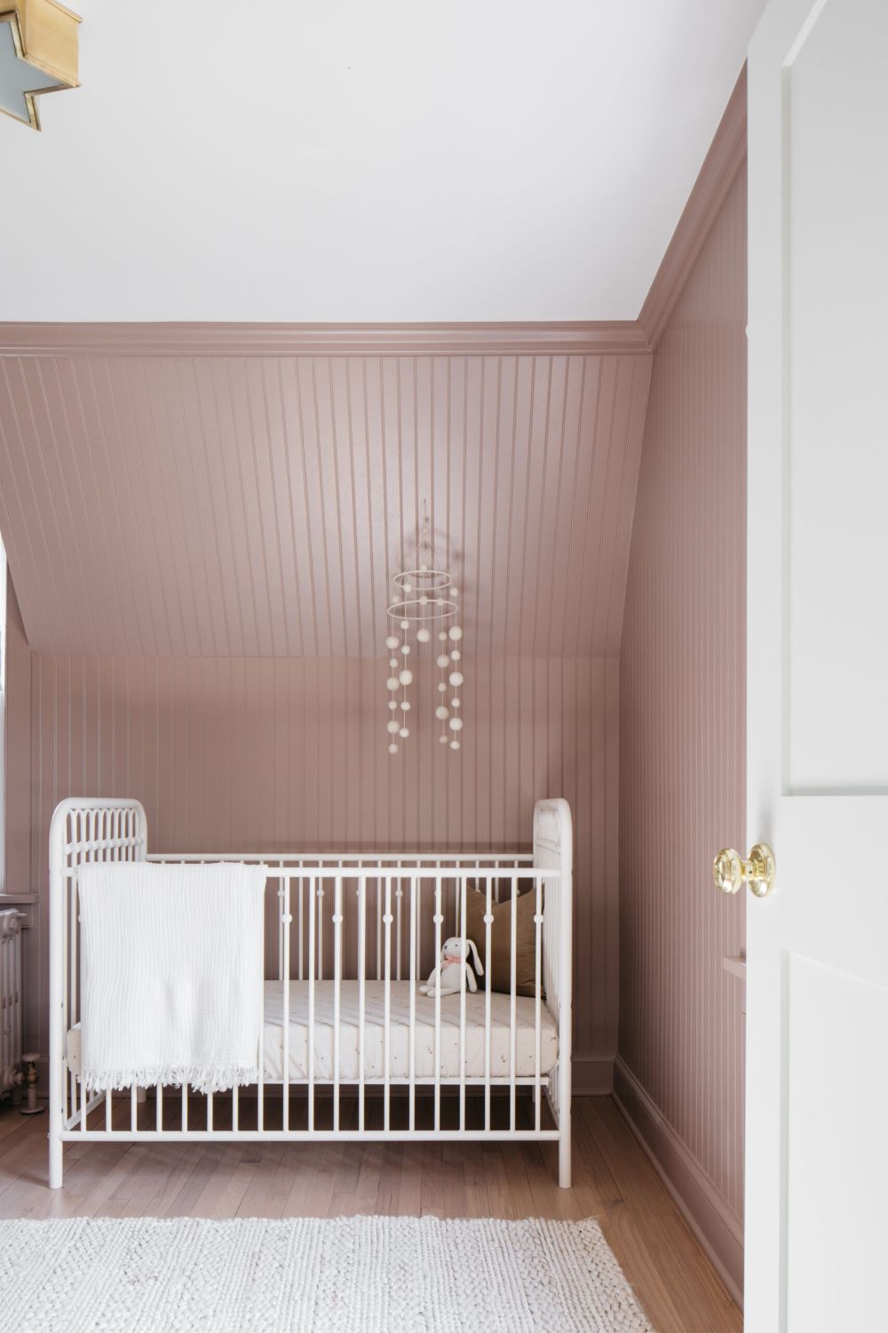 A nursery with soft pink walls, a white crib, and classic decor pieces