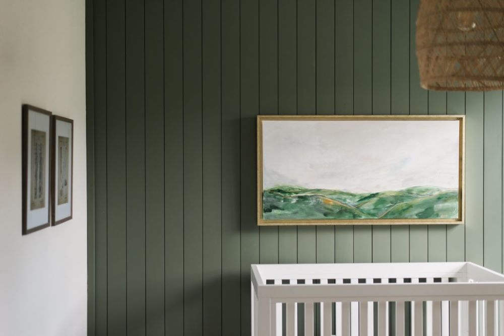 A nursery with dark green walls, a white crib, and boho decor pieces