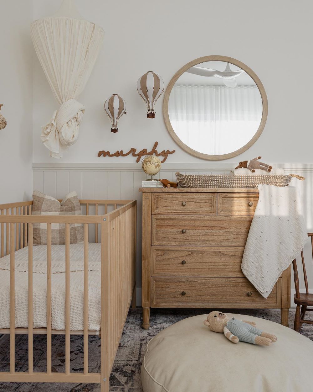 A nursery with white walls and beige board and batten with wood furniture and vintage decor