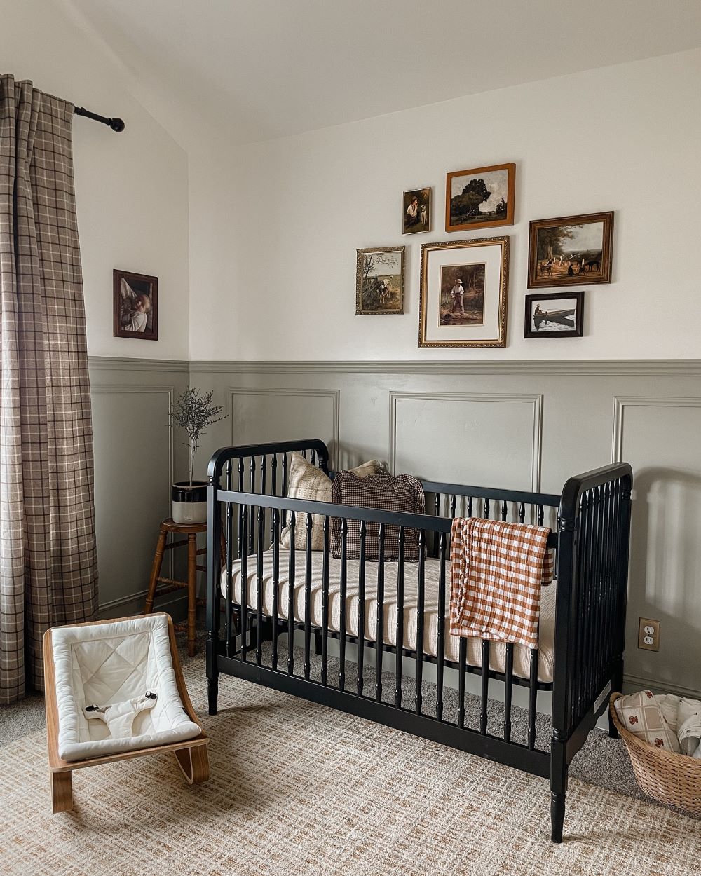 A nursery with soft green walls, a black crib, and vintage decor pieces