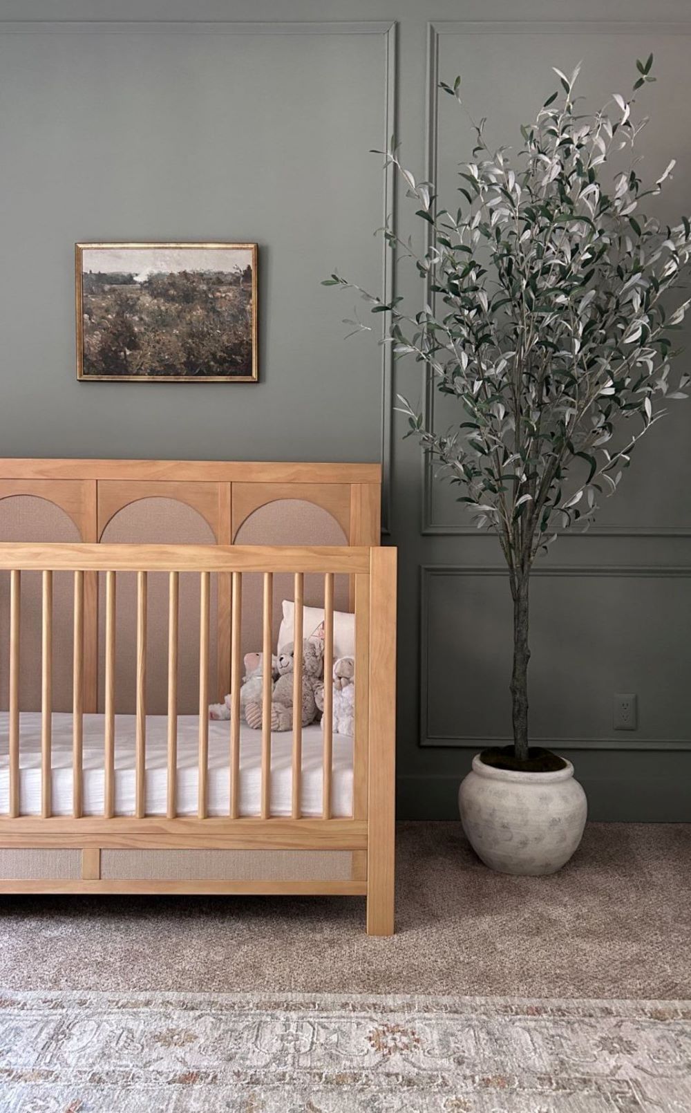 A nursery with dark green walls, a light wood crib, and classic decor pieces