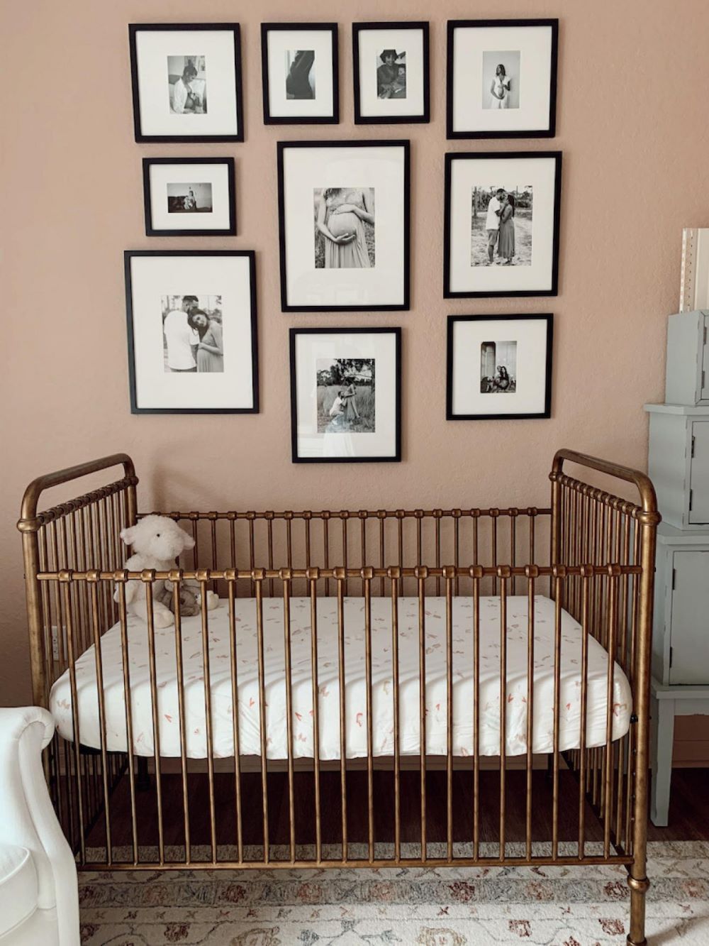 A nursery with soft pink walls, a vintage brass crib, and a gallery wall with family photos