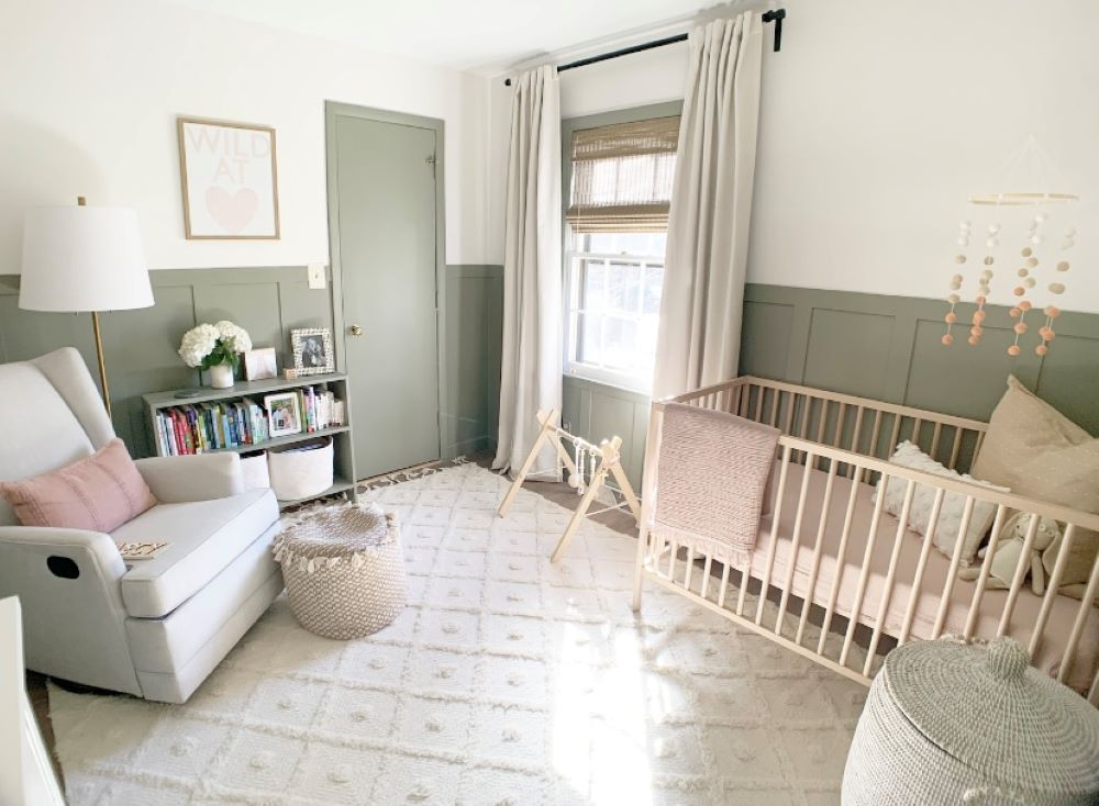 A nursery with white walls and soft green board and batten, a light wood crib, and classic decor pieces