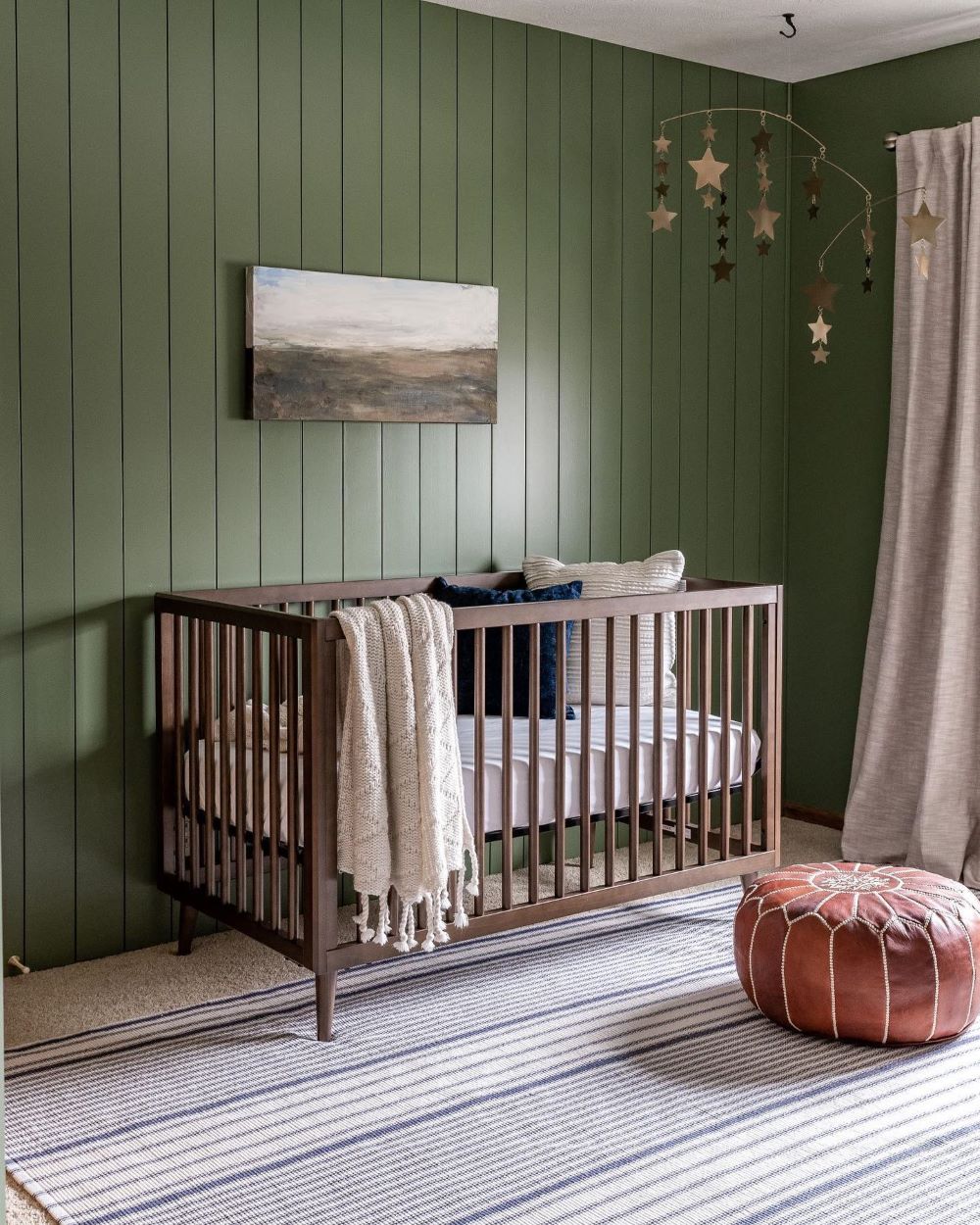 A nursery with earthy green walls, a dark wood crib, and classic decor pieces