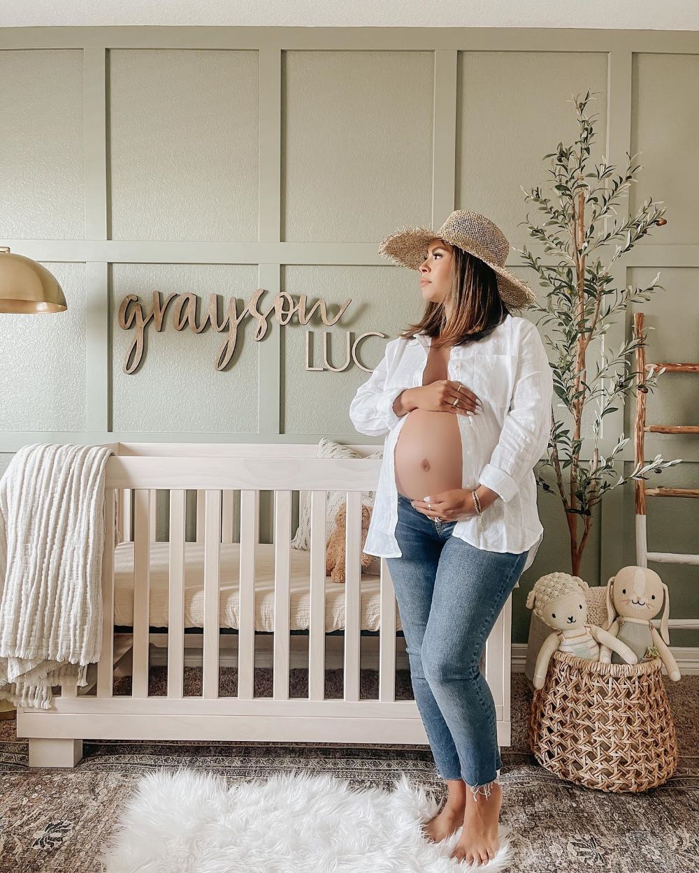 A nursery with sage green paint, a white crib, and natural decor pieces