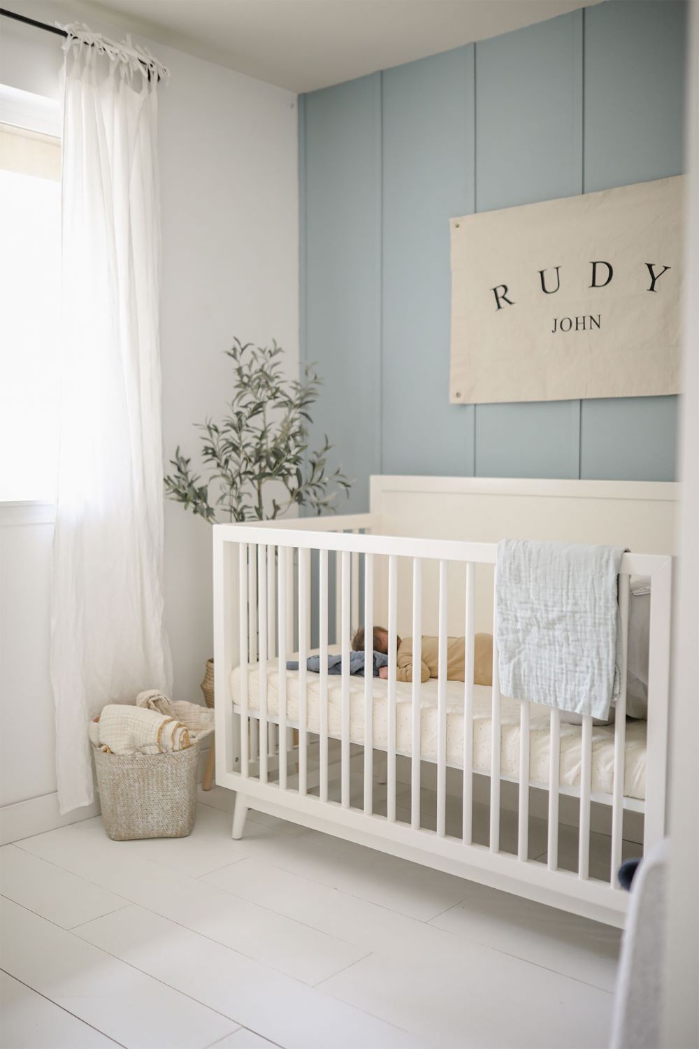 A nursery with dusty blue walls, a white crib, and classic decor pieces