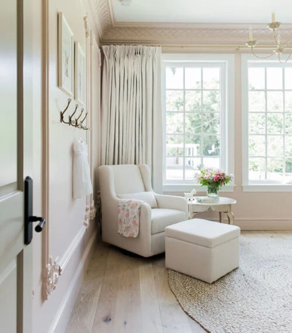 A nursery with soft pink walls, white furniture, and classic decor pieces
