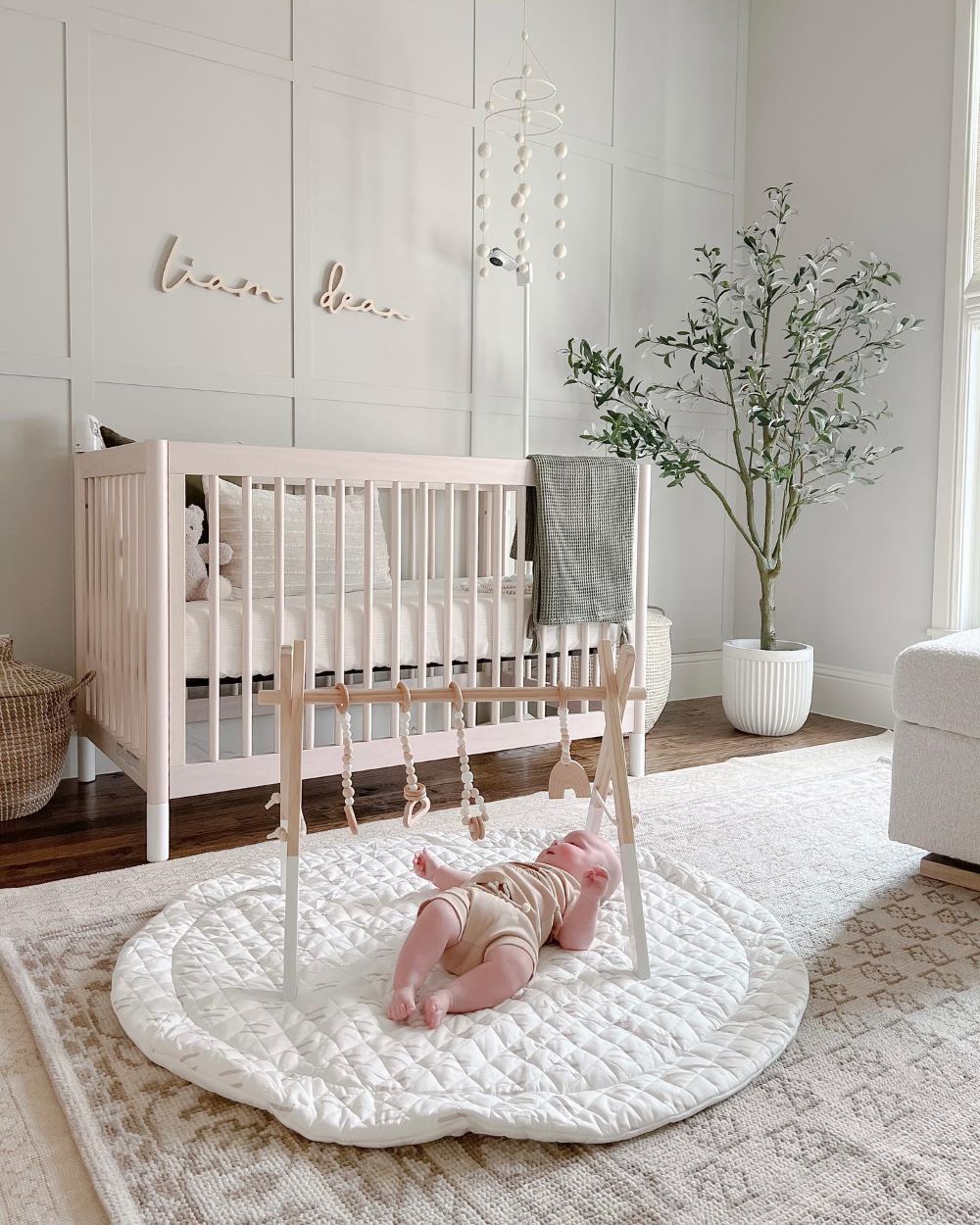 A nursery with soft green walls, a light wood crib, and boho decor pieces