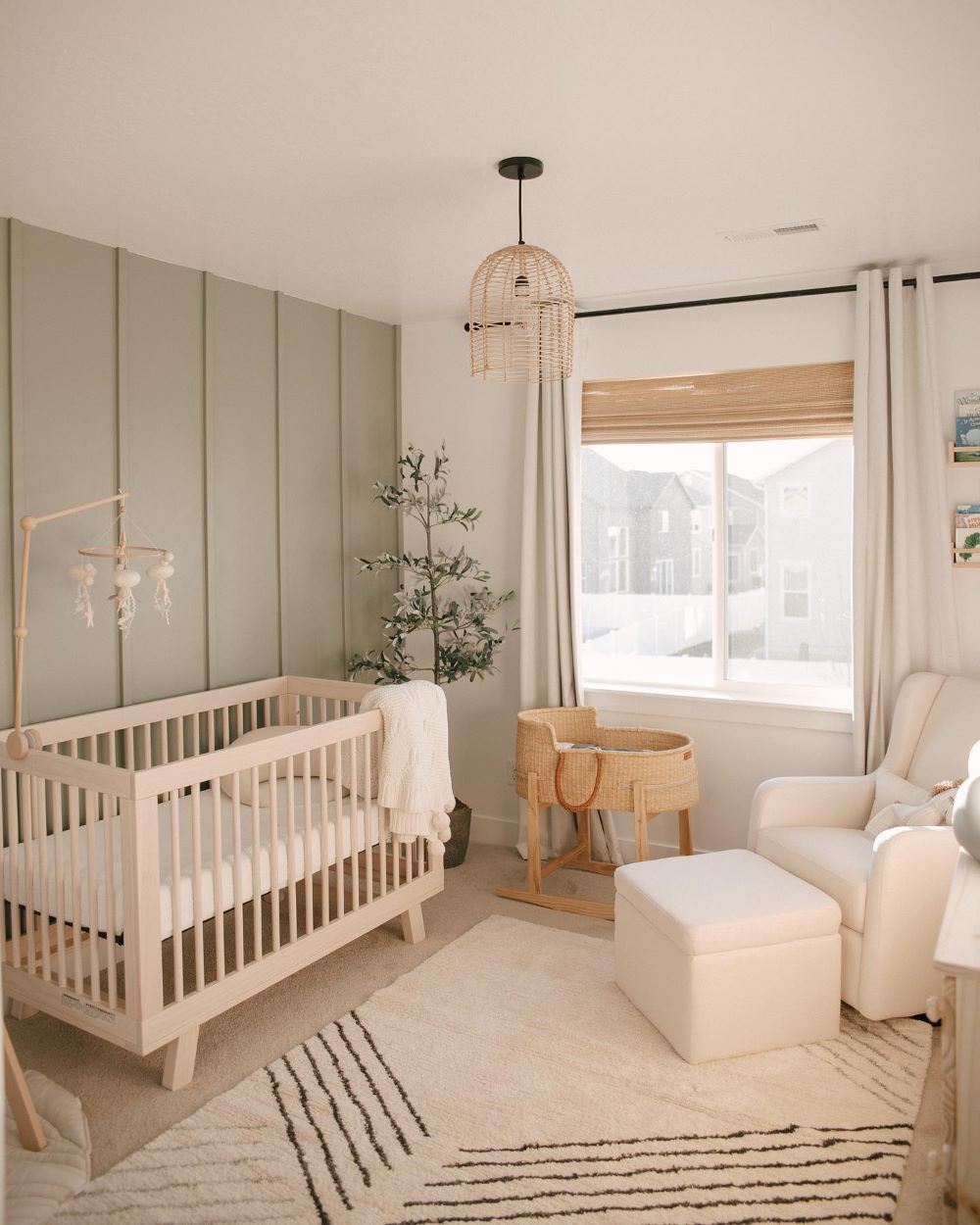 A nursery with soft green and white walls, a light wood crib, and boho decor pieces