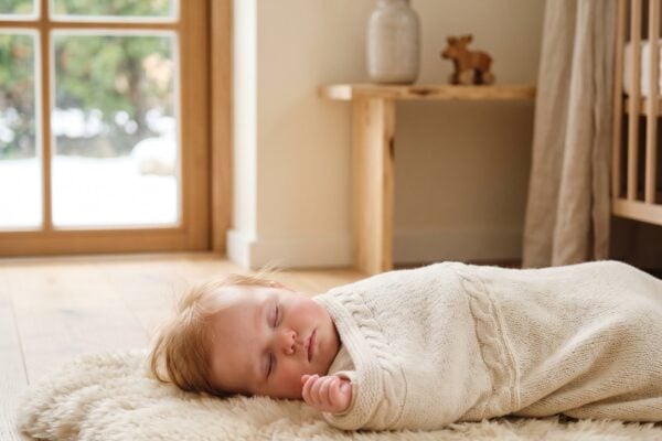 Scandinavian baby girl wrapped in cream knit blanket on sheepskin rug in minimalist Nordic nursery