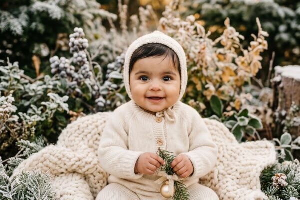 Baby in a frost-covered garden with evergreen branches and soft golden light — Christmas Baby Names for Your Holiday Babe