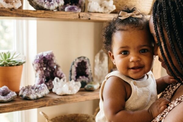 Baby Girl in a sunlit room with geodes and crystals on wooden shelves — 250+ Gemstone and Crystal Baby Names for Your Precious Little One