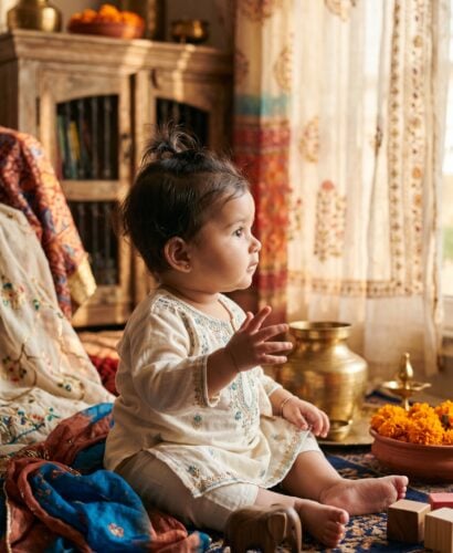 Baby Girl in a sunlit living room with layered traditional Indian textiles — 200+ Indian Baby Girl Names Spanning Every Region and Tradition
