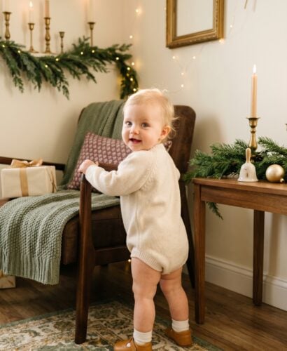 Baby in a cream-walled corner styled with soft evergreen and warm gold — Noel-Inspired Baby Names for December Babies