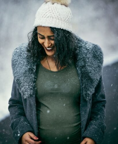 Pregnant woman smiling in falling snow for a winter maternity photoshoot