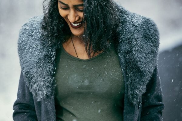Pregnant woman smiling in falling snow for a winter maternity photoshoot