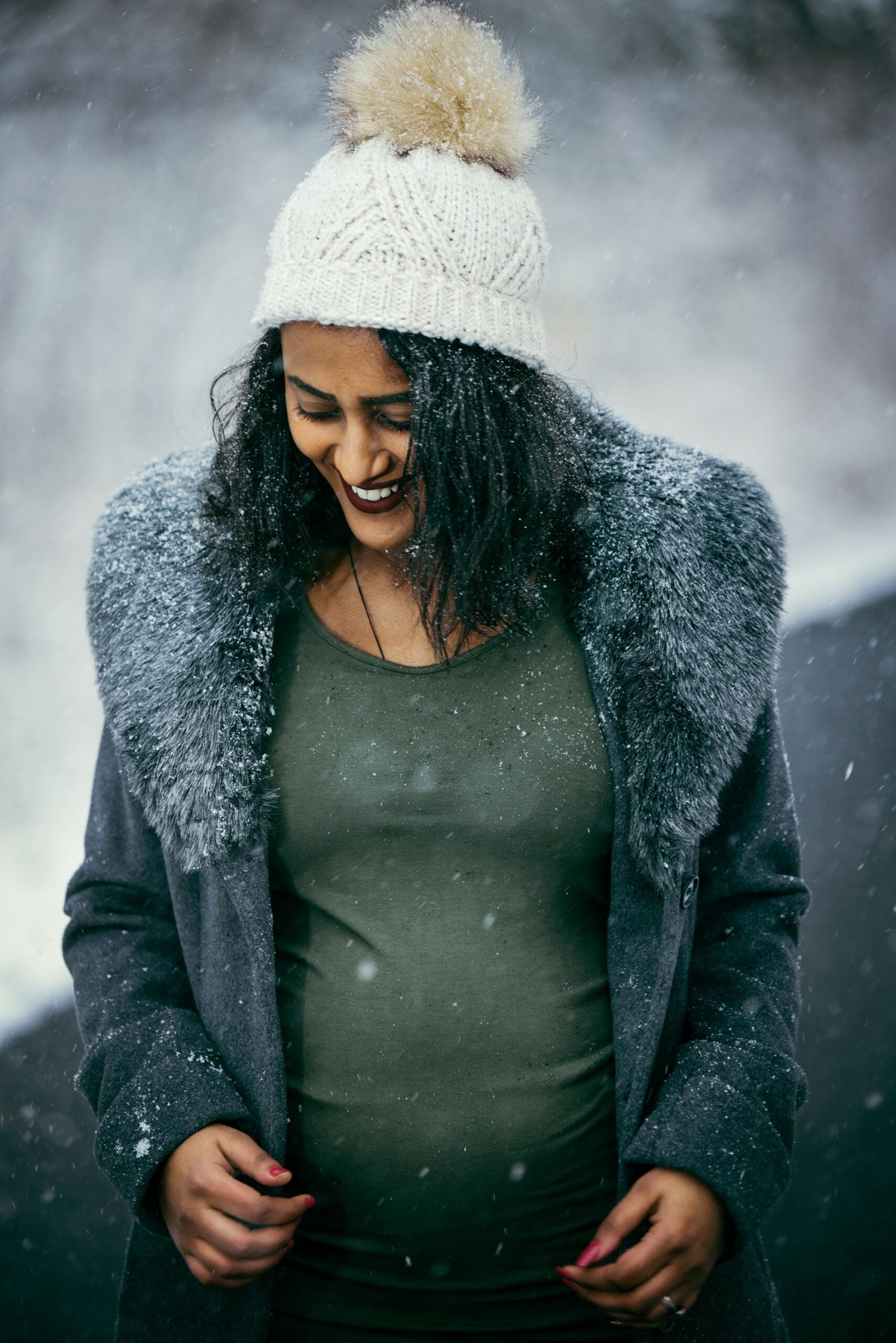 Pregnant woman smiling in falling snow for a winter maternity photoshoot