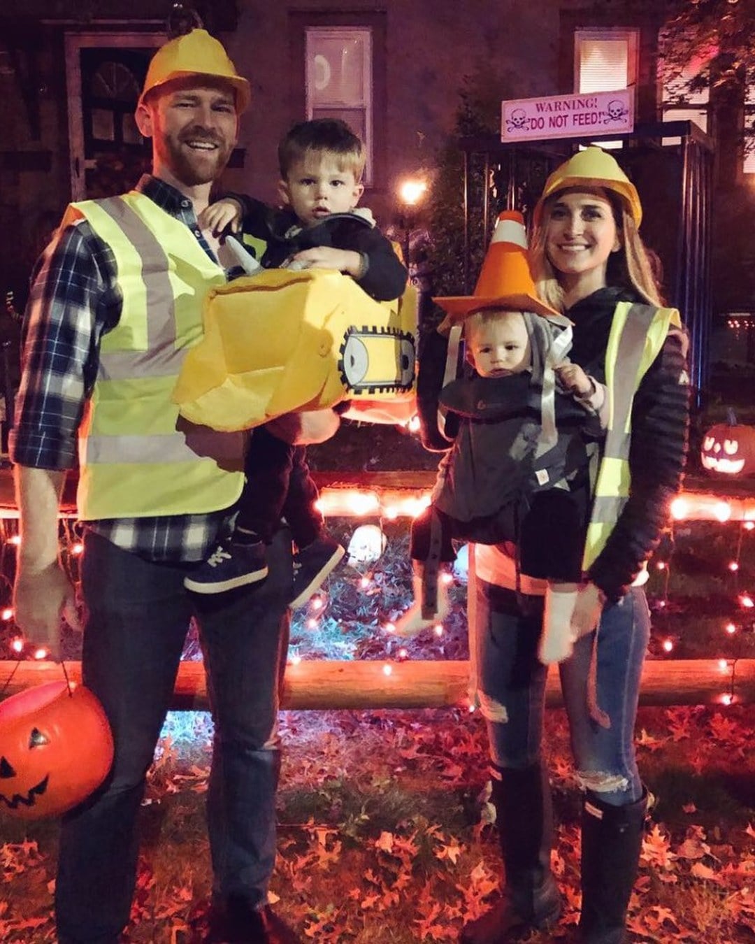 A mom and dad with three kids dressed as a construction crew, including a digger costume, a hard-hatted worker, and an orange traffic cone, all made from cardboard and safety vests.