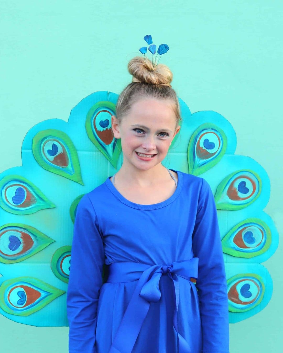 Baby in a blue and green tulle peacock tutu with a spray-painted cardboard tail piece and feathered headband.