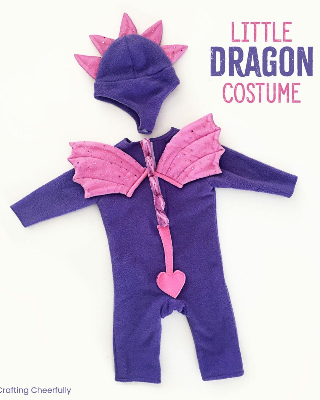 Baby wearing a purple fleece dragon costume with sparkly pink wings and soft spikes down the hood and spine.
