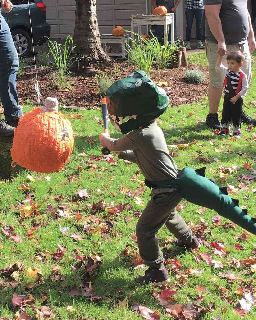 Baby in a green felt-spiked dinosaur costume wearing a paper-mache T-Rex head like a hat.