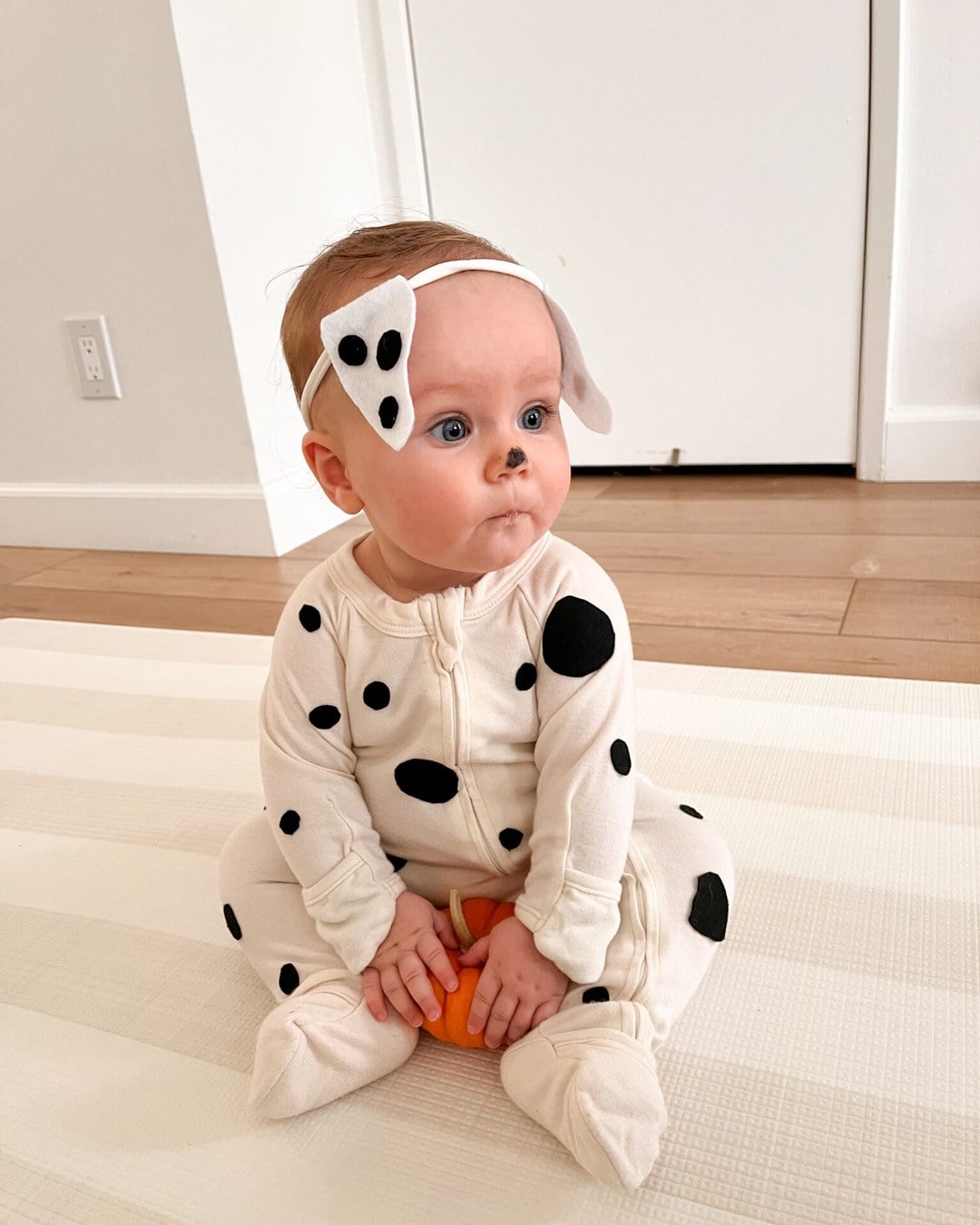 Baby in a white onesie covered in hand-cut black felt spots, wearing a fleece puppy-ear headband.