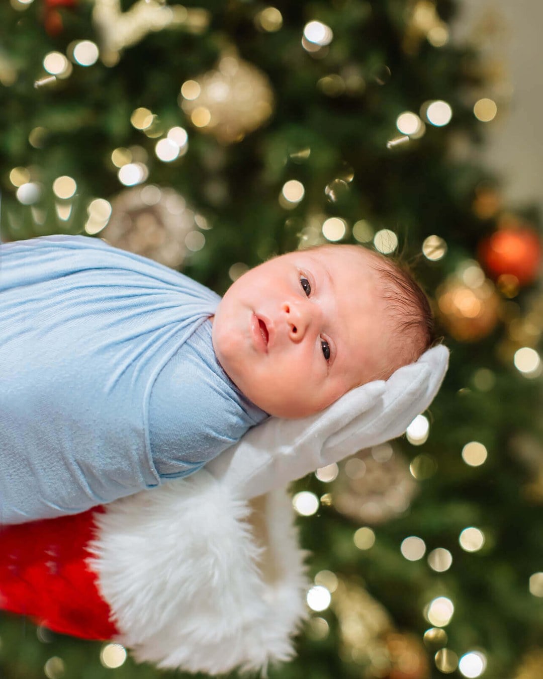 A hand wrapped in red and white stocking fabric, styled to look like Santa's sleeve, reaching in to hold a baby.