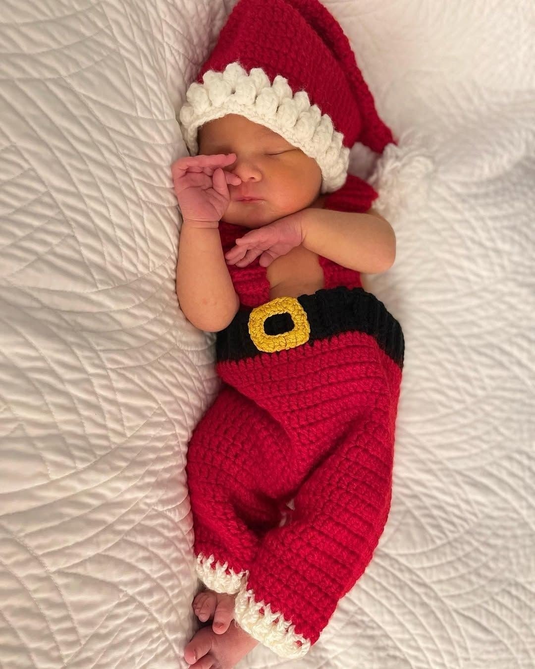 A newborn dressed in a full hand-knitted Santa suit with jacket, trousers, and boots.