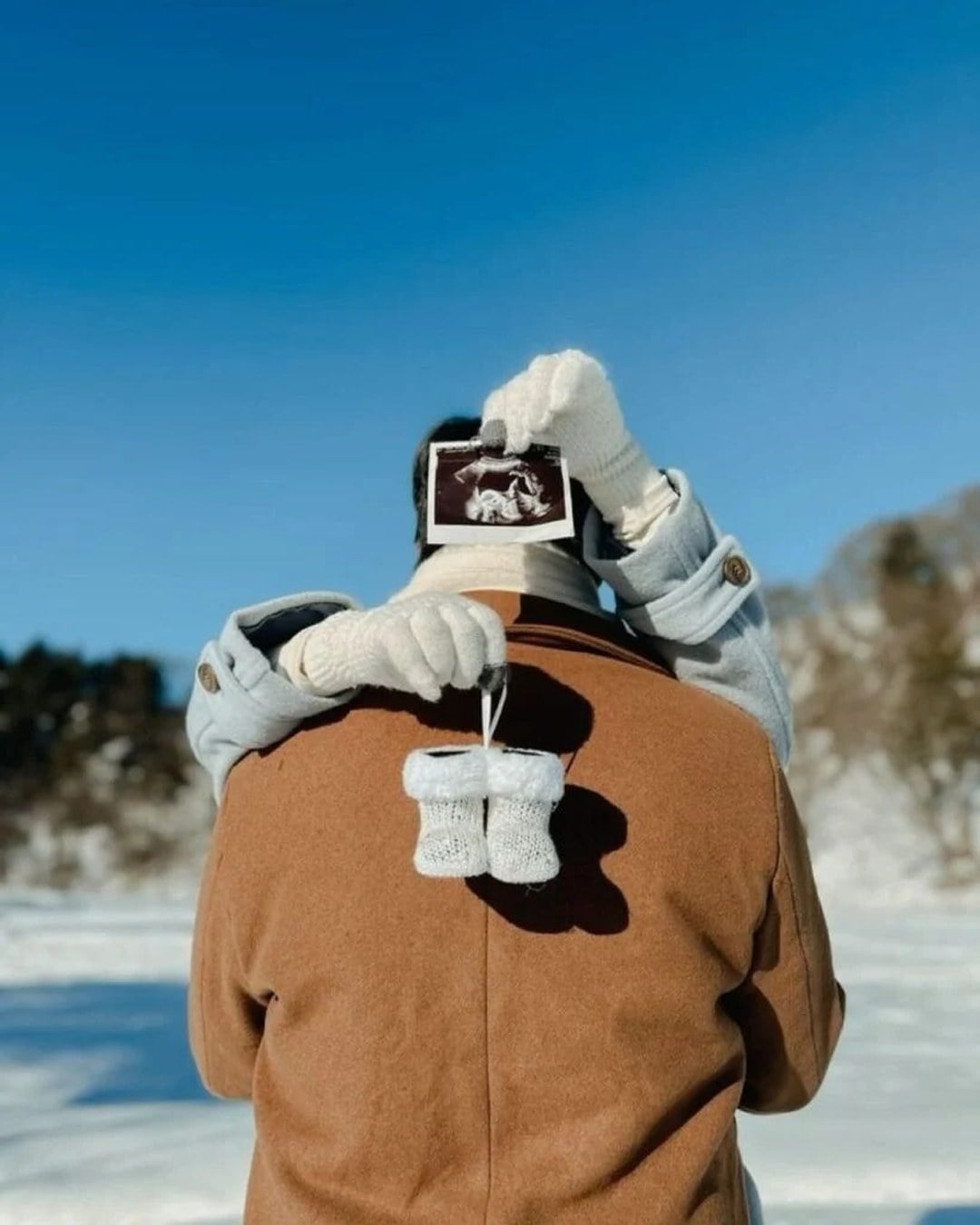 Sonogram photo styled next to tiny winter baby booties in the snow