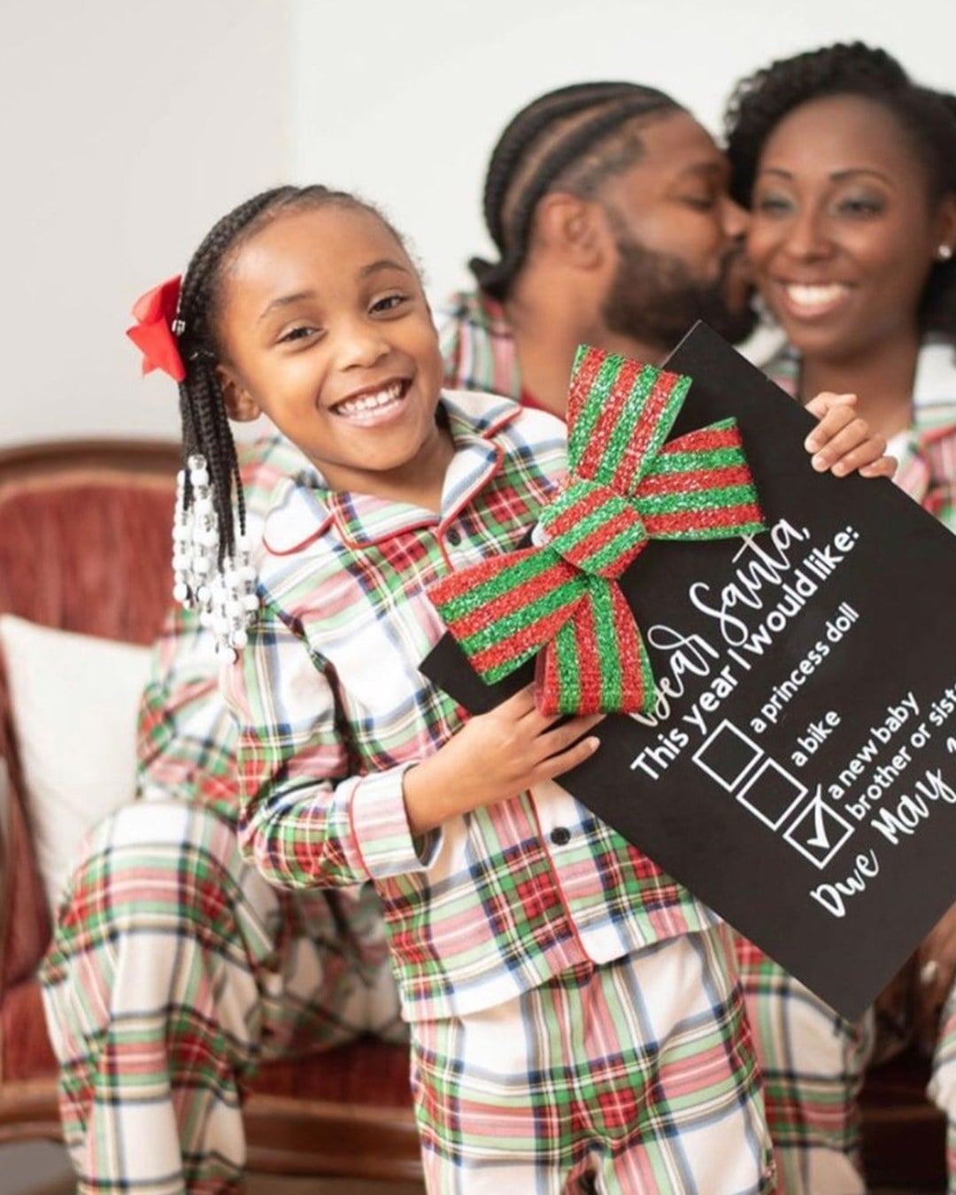 Young child holding a chalkboard Dear Santa wish list with 'a little sibling' written as the last item