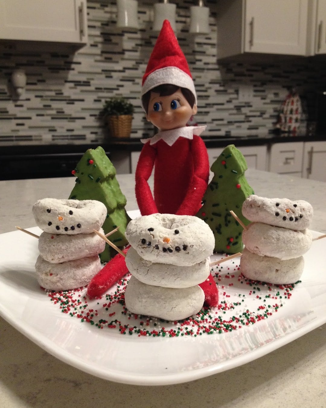 Elf on the Shelf surrounded by donut hole snowmen and mini Christmas tree snack cakes