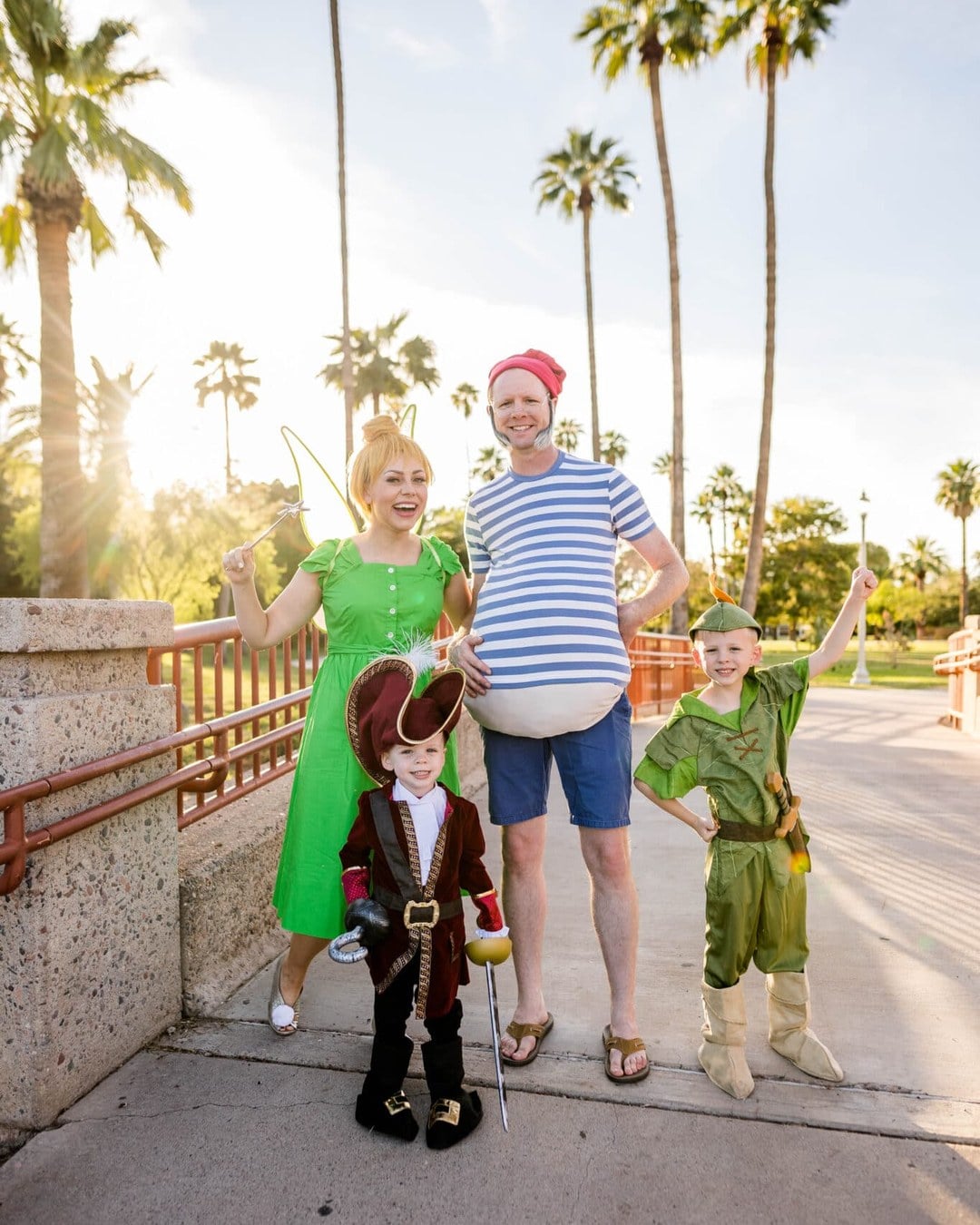 Family dressed as Peter Pan, Wendy, Tinker Bell, and Captain Hook outdoors, with Hook's costume styled as half-crocodile