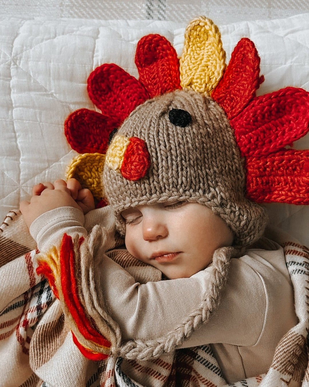 Knit turkey hat with red and yellow feathers, a beak, a wattle and braided earflap ties