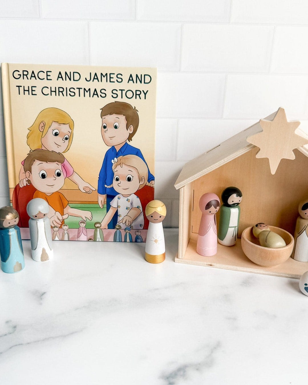 A wooden nativity house with painted peg-doll figures next to a children's Christmas story book