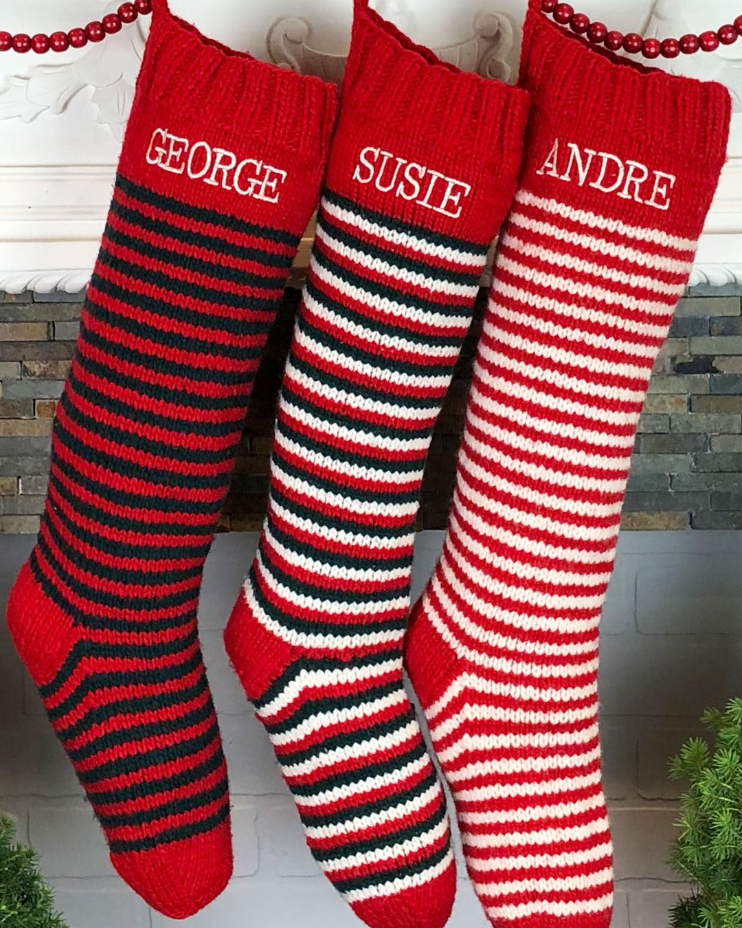 Three hand-knit red striped Christmas stockings with names, hung from a white mantel