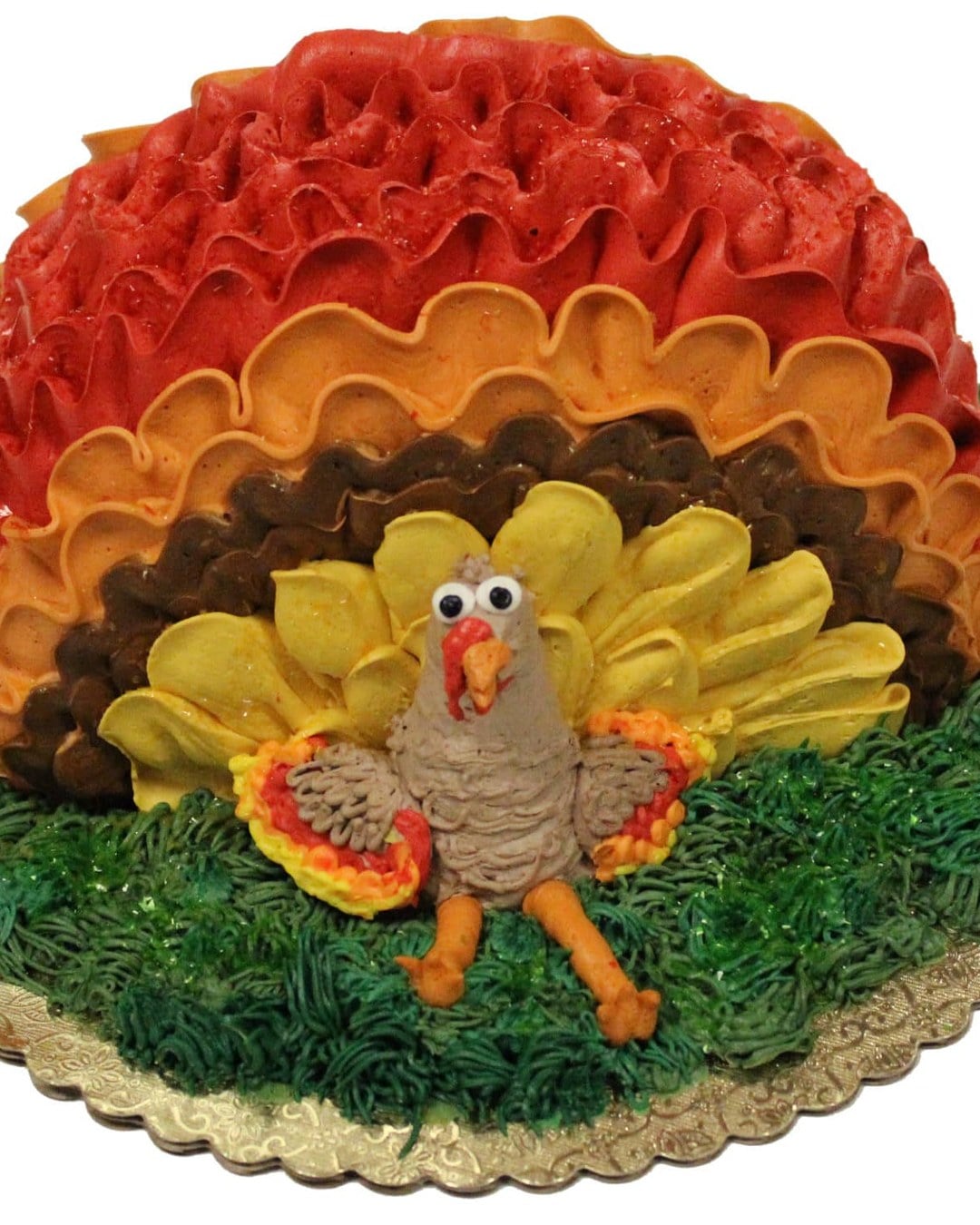 Bakery cake shaped as a turkey with red, orange, brown and yellow buttercream ruffle feathers on a gold board