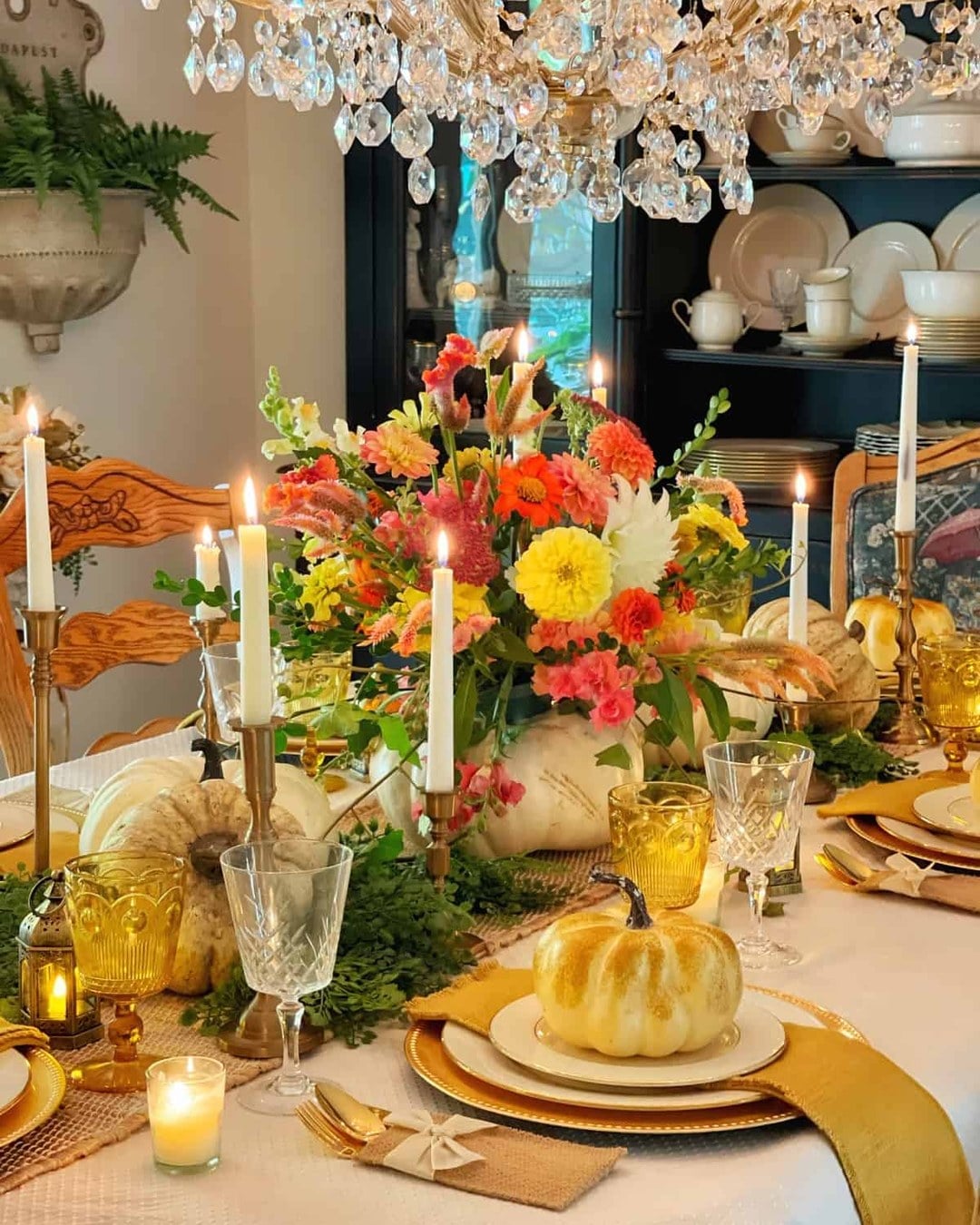Candlelit dining table with a dahlia and zinnia centerpiece in a white pumpkin, taper candles and a burlap runner