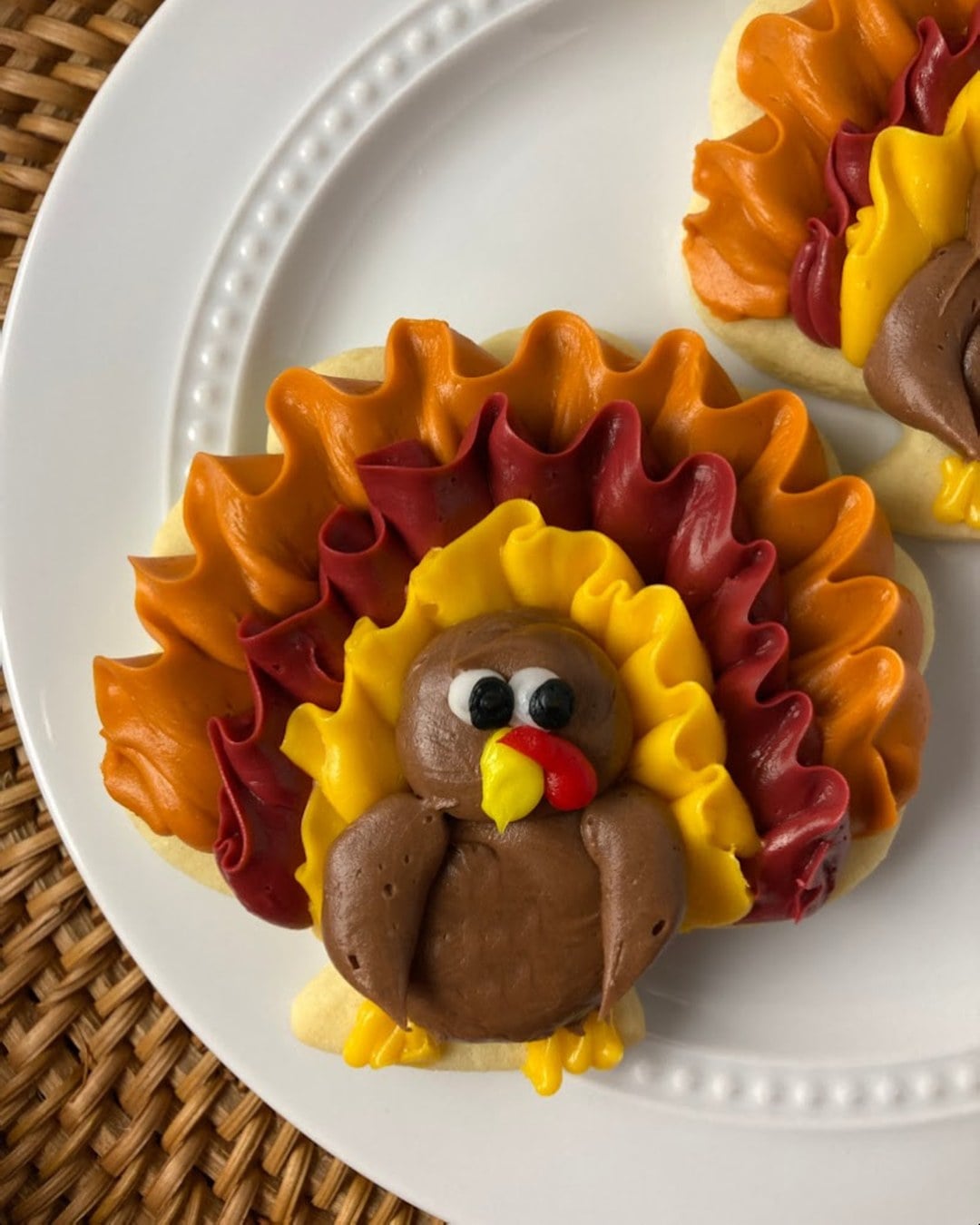Buttercream-decorated turkey cookie with orange, red and yellow feathers on a white plate