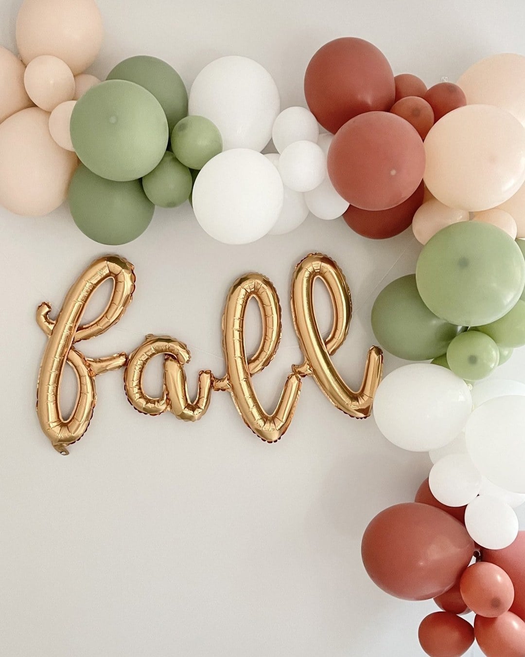 Organic balloon garland in blush, sage, white and terracotta wrapping a white wall with a gold foil 'fall' balloon